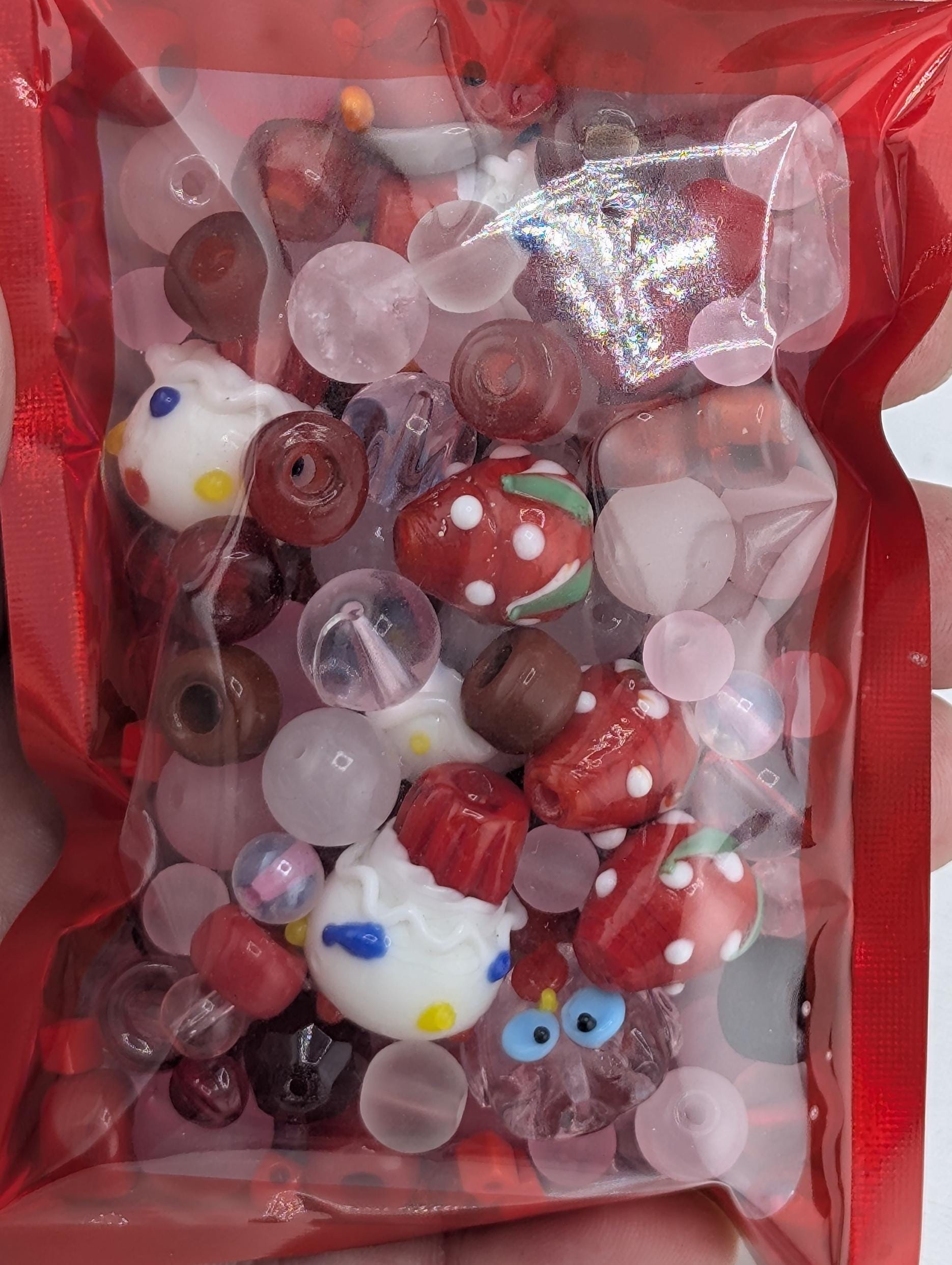 A red plastic bag filled with various colorful beads, including clear beads and beads with polka dots, as well as some small plastic figurines.