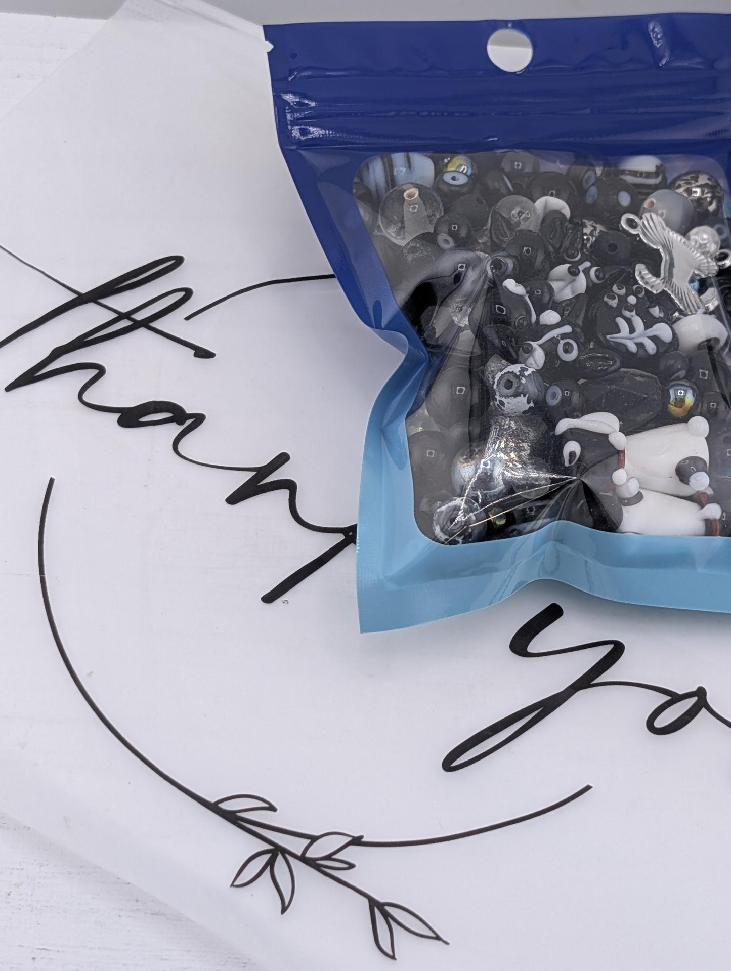 A package of black and white toy figurines is shown on a white surface, with a blue and white &quot;Thank you&quot; sign in the background.