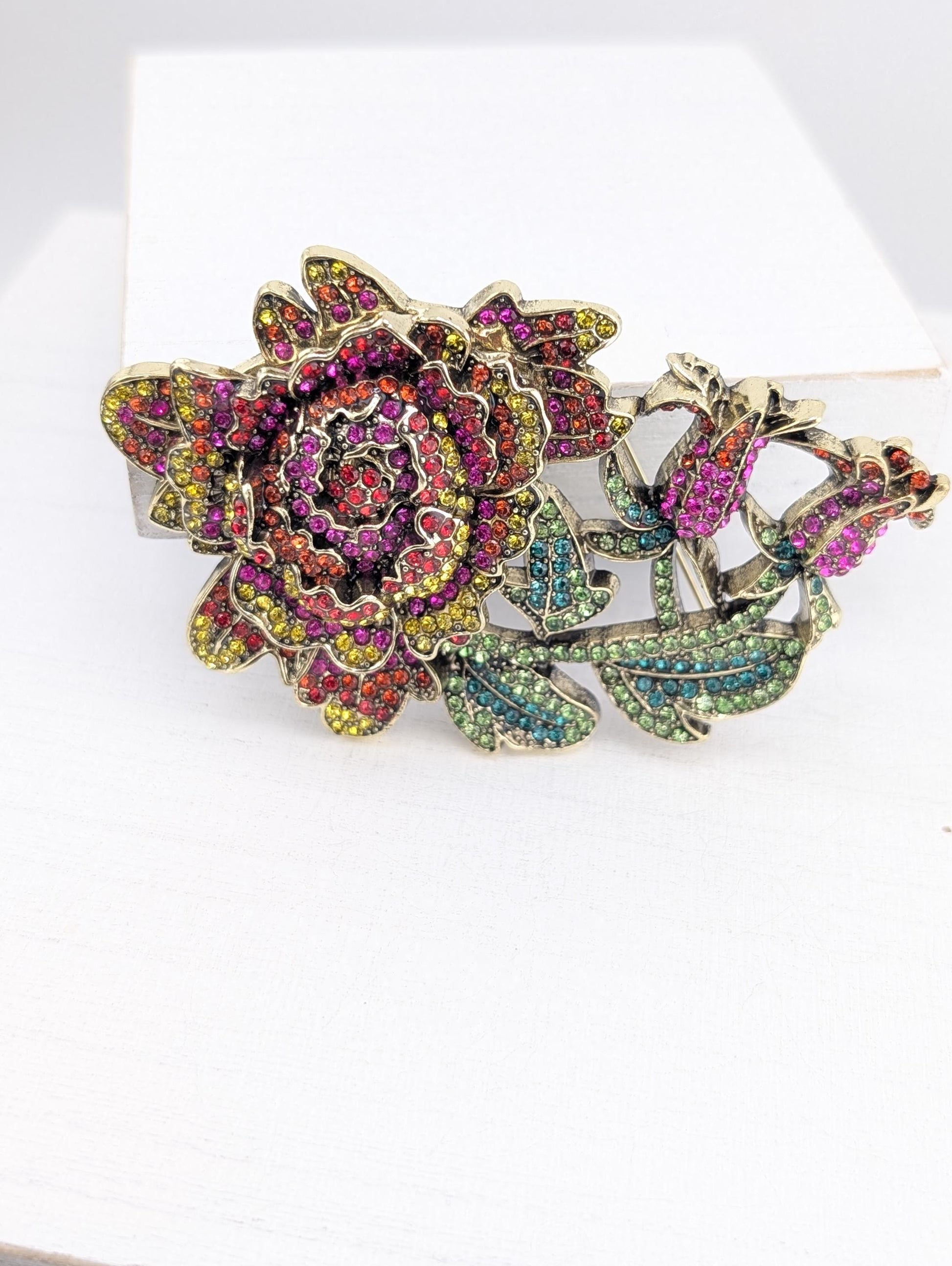 A decorative brooch with a large, colorful flower design and various gemstones.