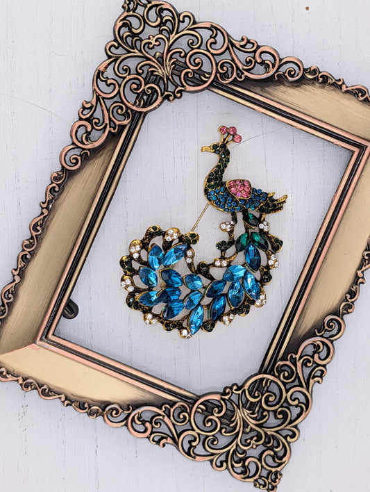 a decorative gold frame with a peacock brooch displayed within it.