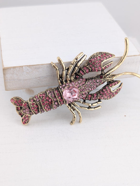 A decorative lobster brooch with a pink gemstone on its body.