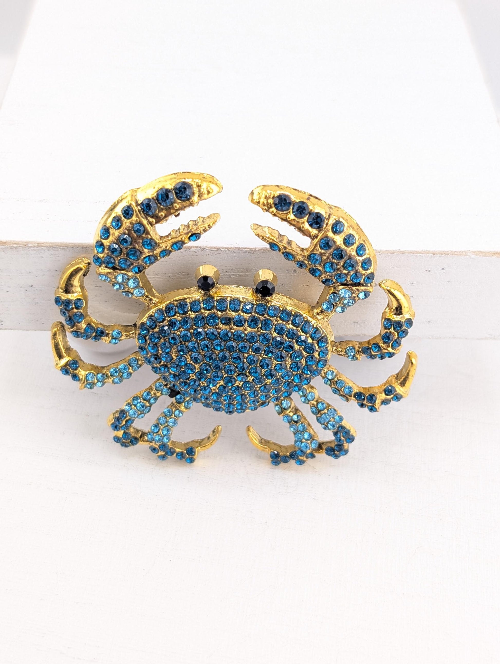 A decorative crab-shaped brooch made of gold and blue rhinestones.