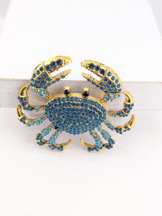A decorative crab-shaped brooch made of gold and blue rhinestones.