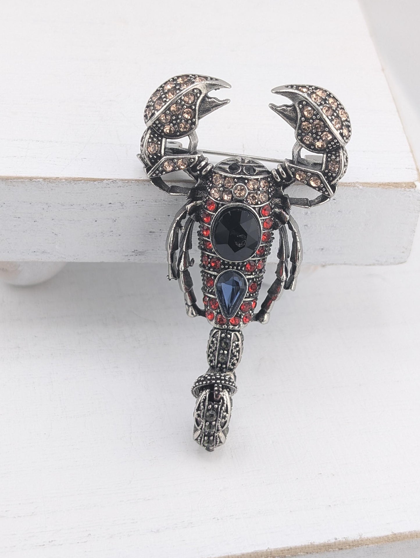A decorative brooch in the shape of a scorpion, adorned with various gemstones and intricate metalwork.