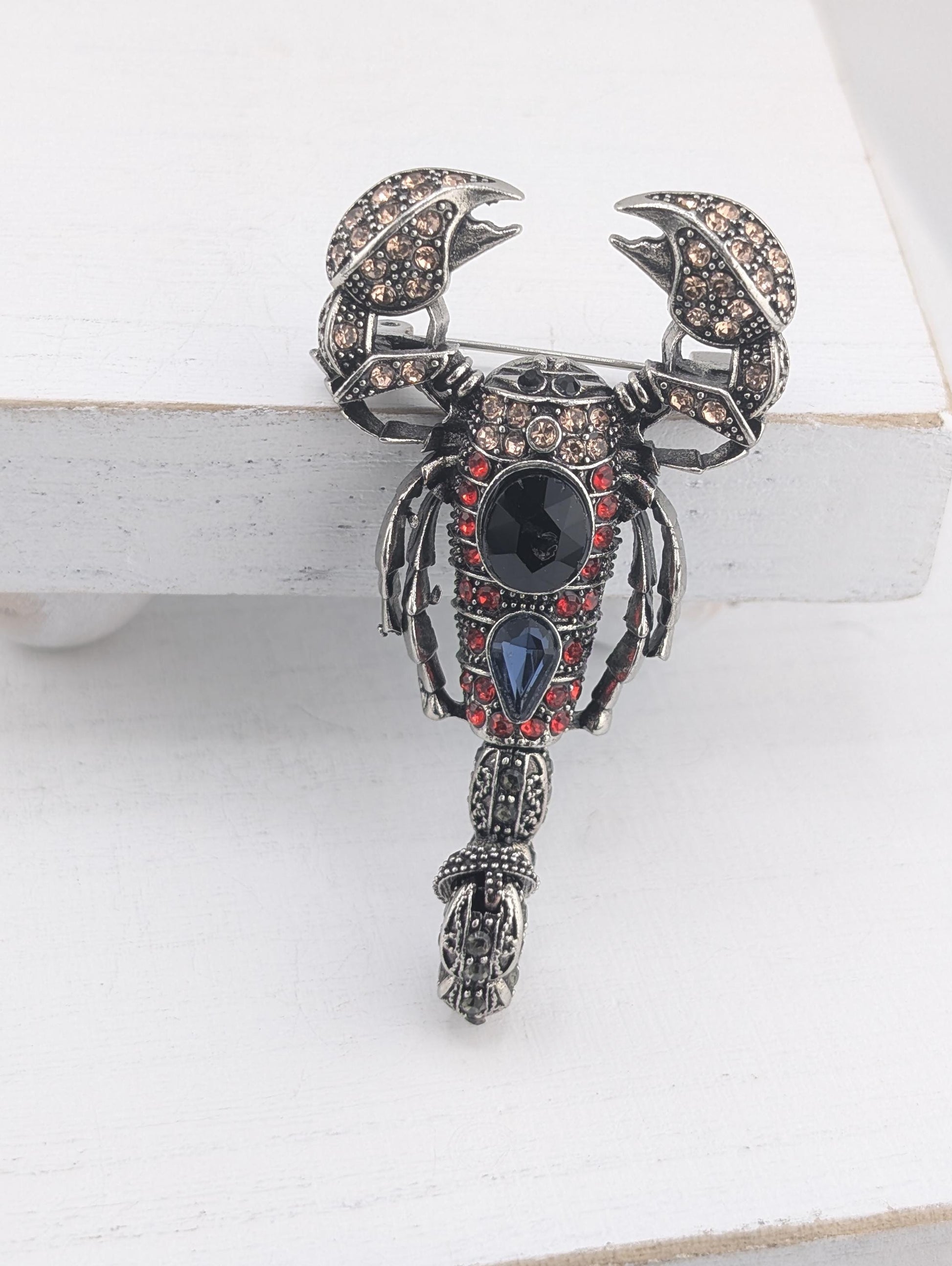 A decorative brooch in the shape of a scorpion, adorned with various gemstones and intricate metalwork.