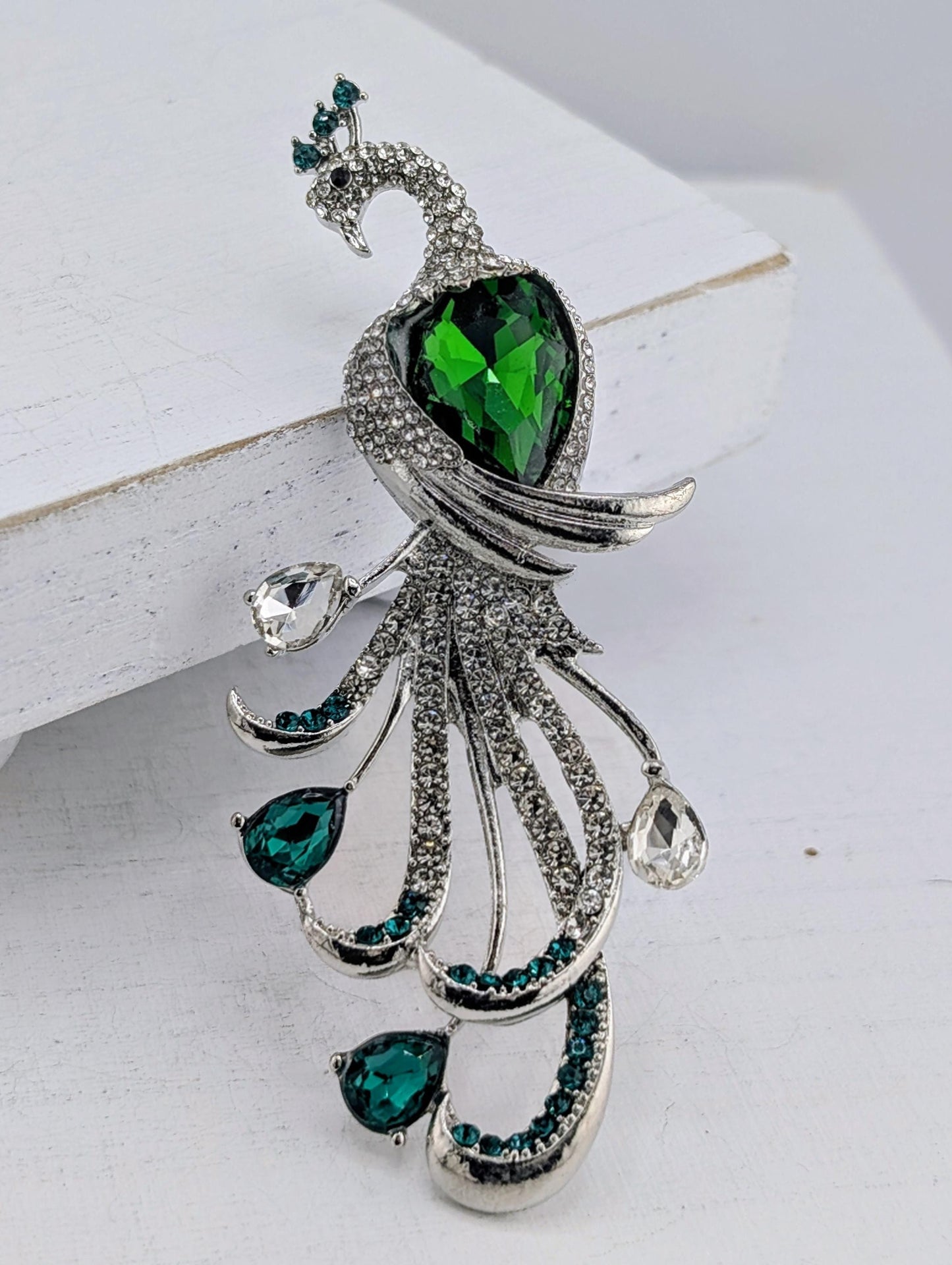 A decorative brooch in the shape of a peacock, adorned with green gemstones and silver details.