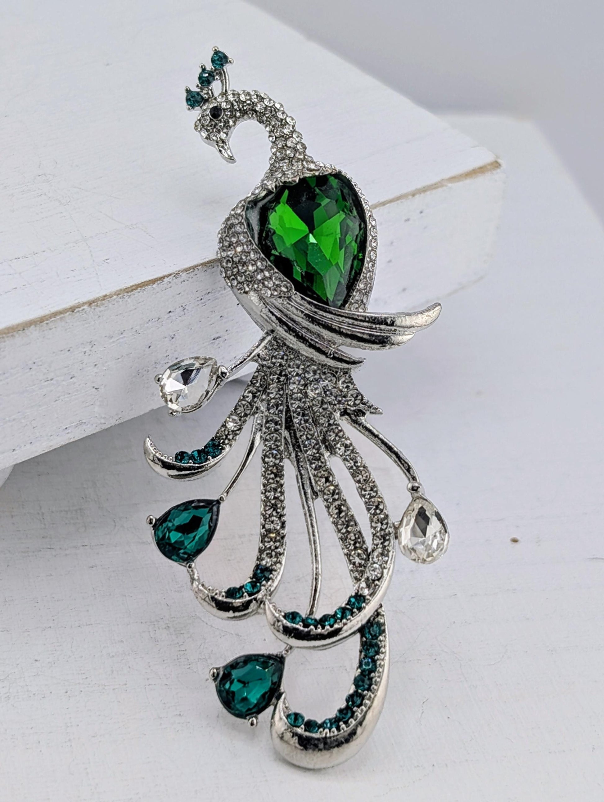 A decorative brooch in the shape of a peacock, adorned with green gemstones and silver details.