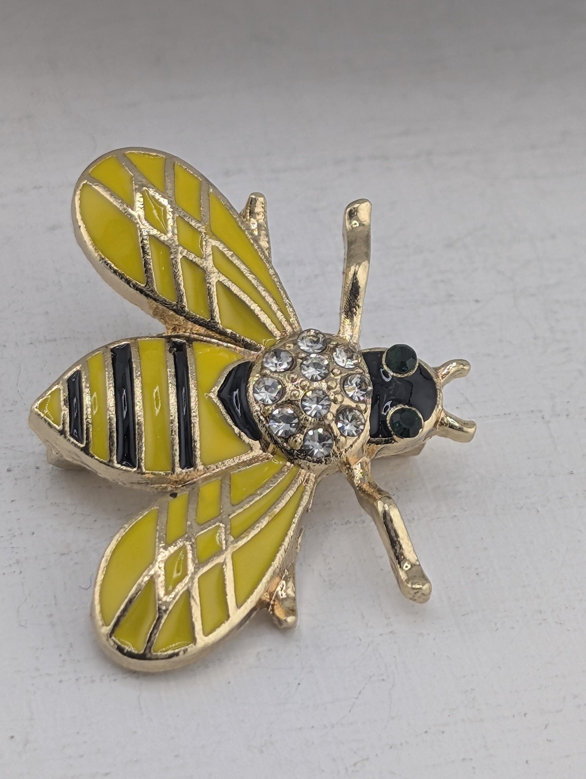 A decorative pin in the shape of a bee, with yellow and black striped wings, a black body, and a gold-colored head.