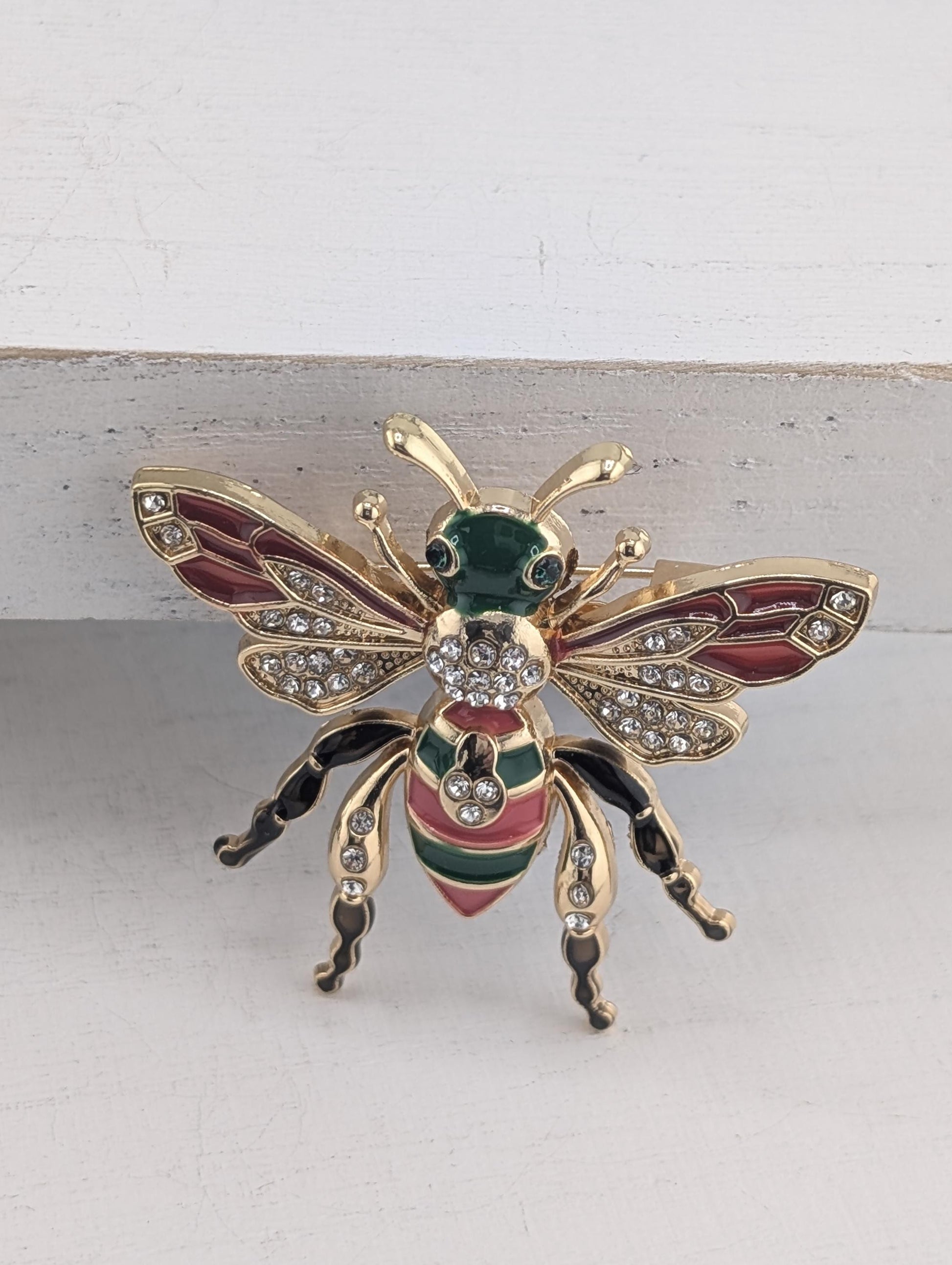 A decorative pin in the shape of a bee, adorned with colorful gemstones and intricate details.