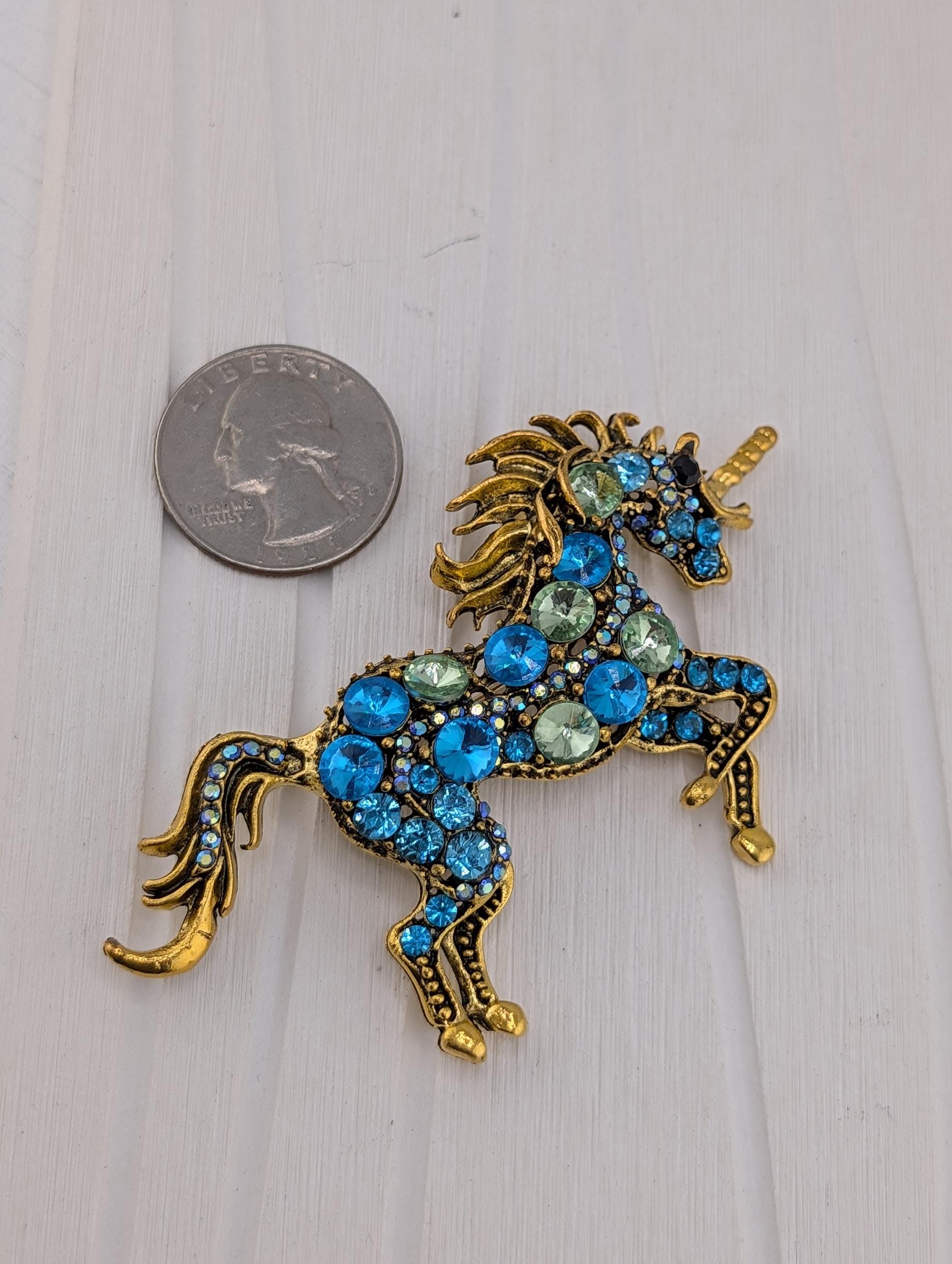 A decorative unicorn brooch made of blue and gold gemstones, placed next to a United States quarter coin.