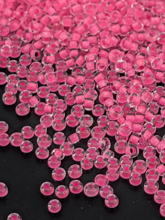 The image is a close-up of numerous small, clear beads in a vibrant shade of pink, scattered across a dark background.