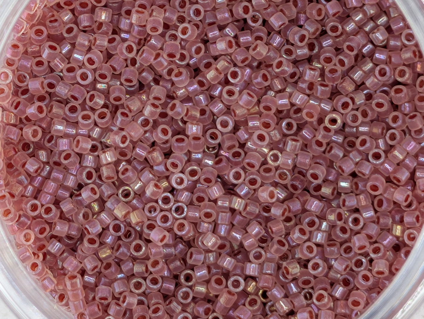 A close-up image of a container filled with numerous small, pink beads.
