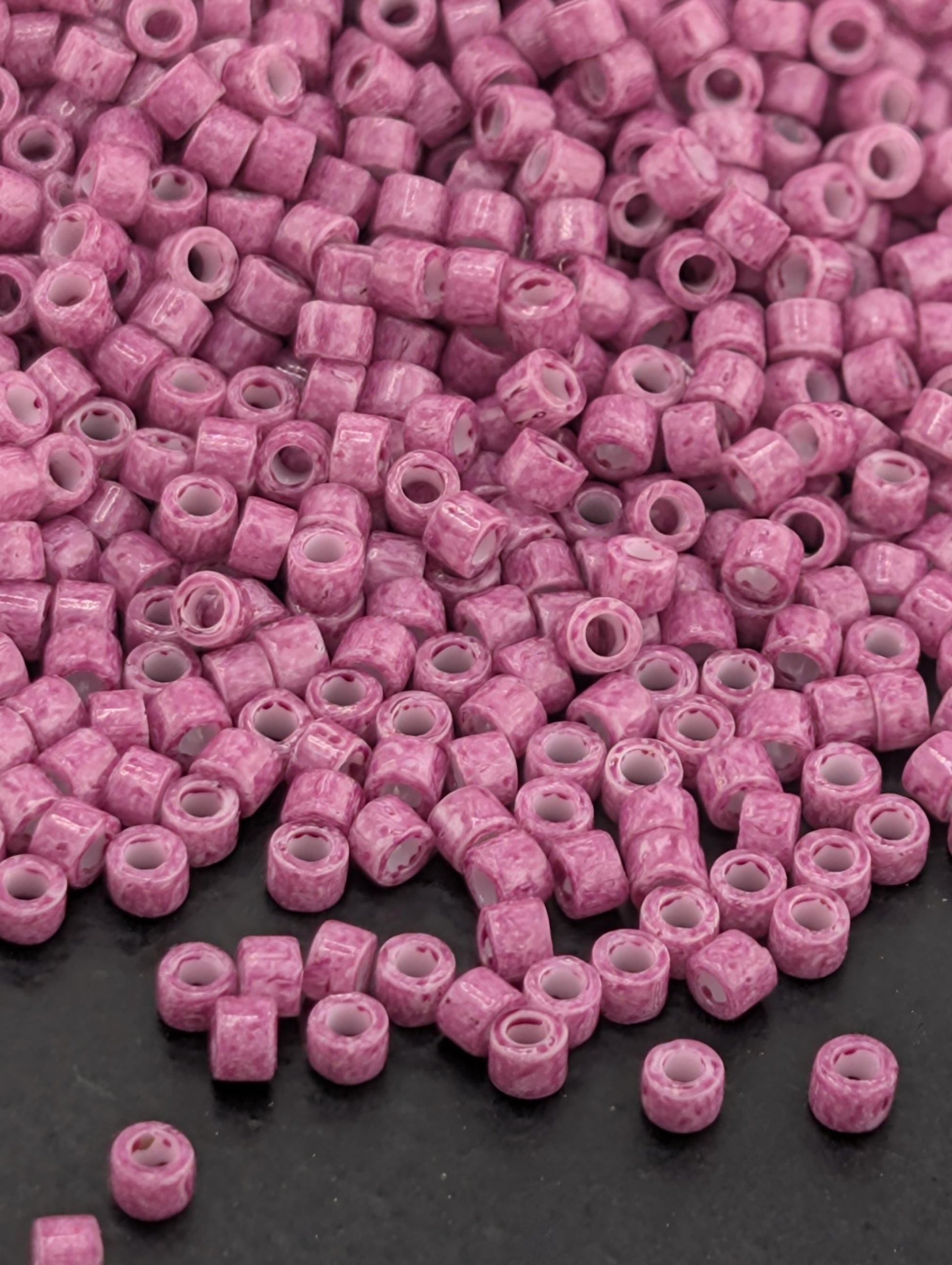 a large pile of small, pink beads scattered on a dark surface.