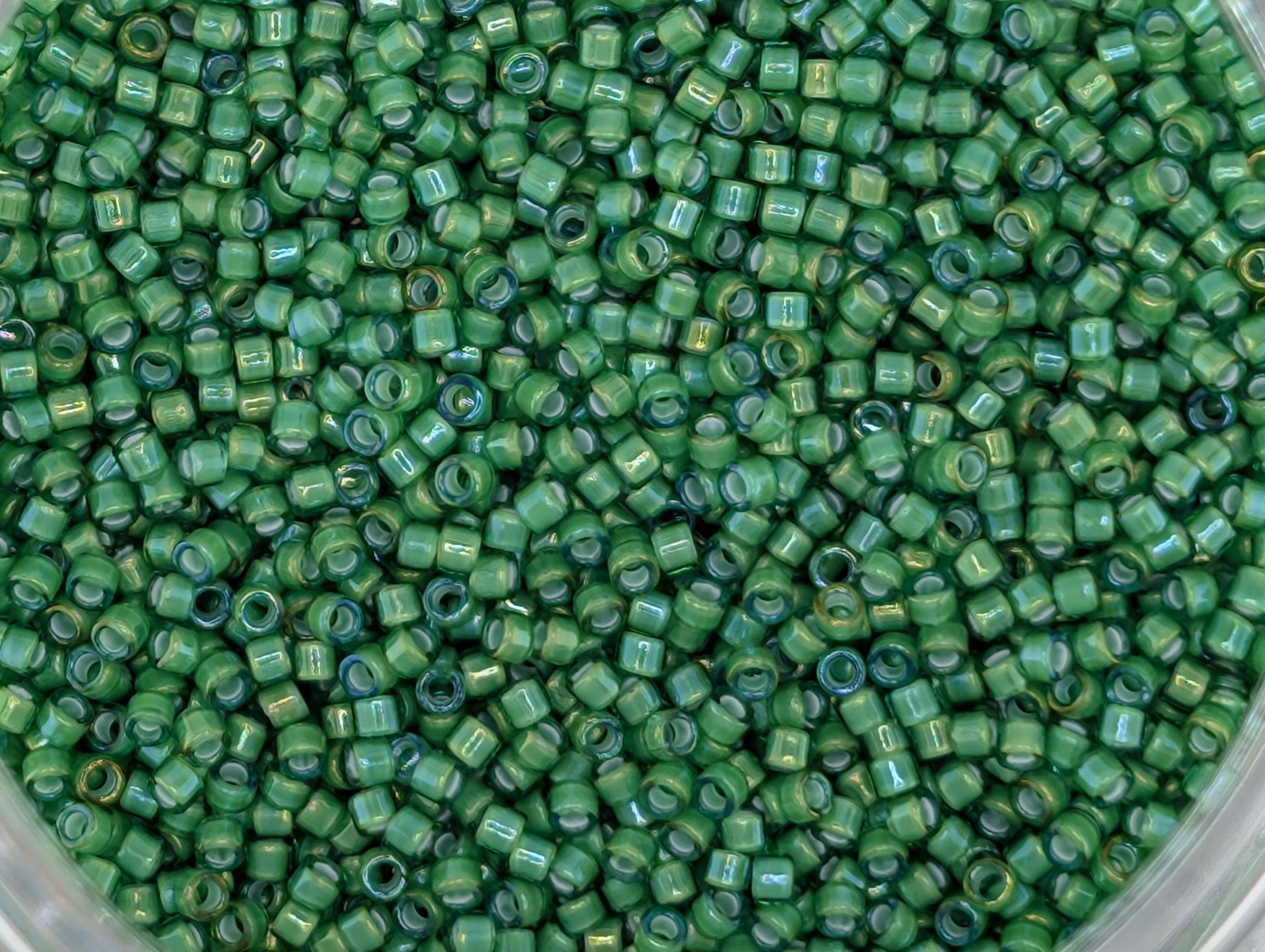 A close-up image of a large pile of green beads or seed beads, with a variety of sizes and shapes.