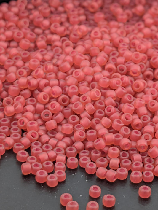 a large pile of small, round, pink beads scattered on a dark surface.