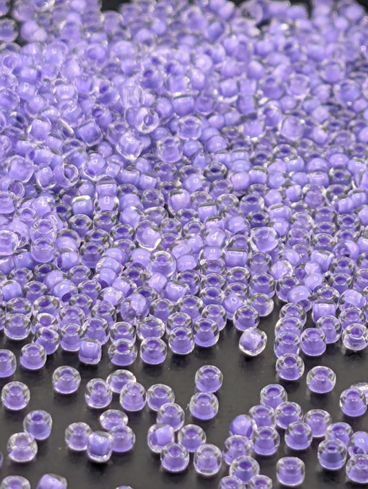 a close-up view of numerous small, clear beads in various shades of purple, scattered across a dark background.