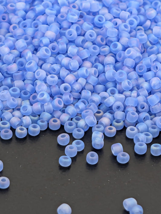 a large pile of small, clear beads in various shades of blue, scattered on a dark surface.