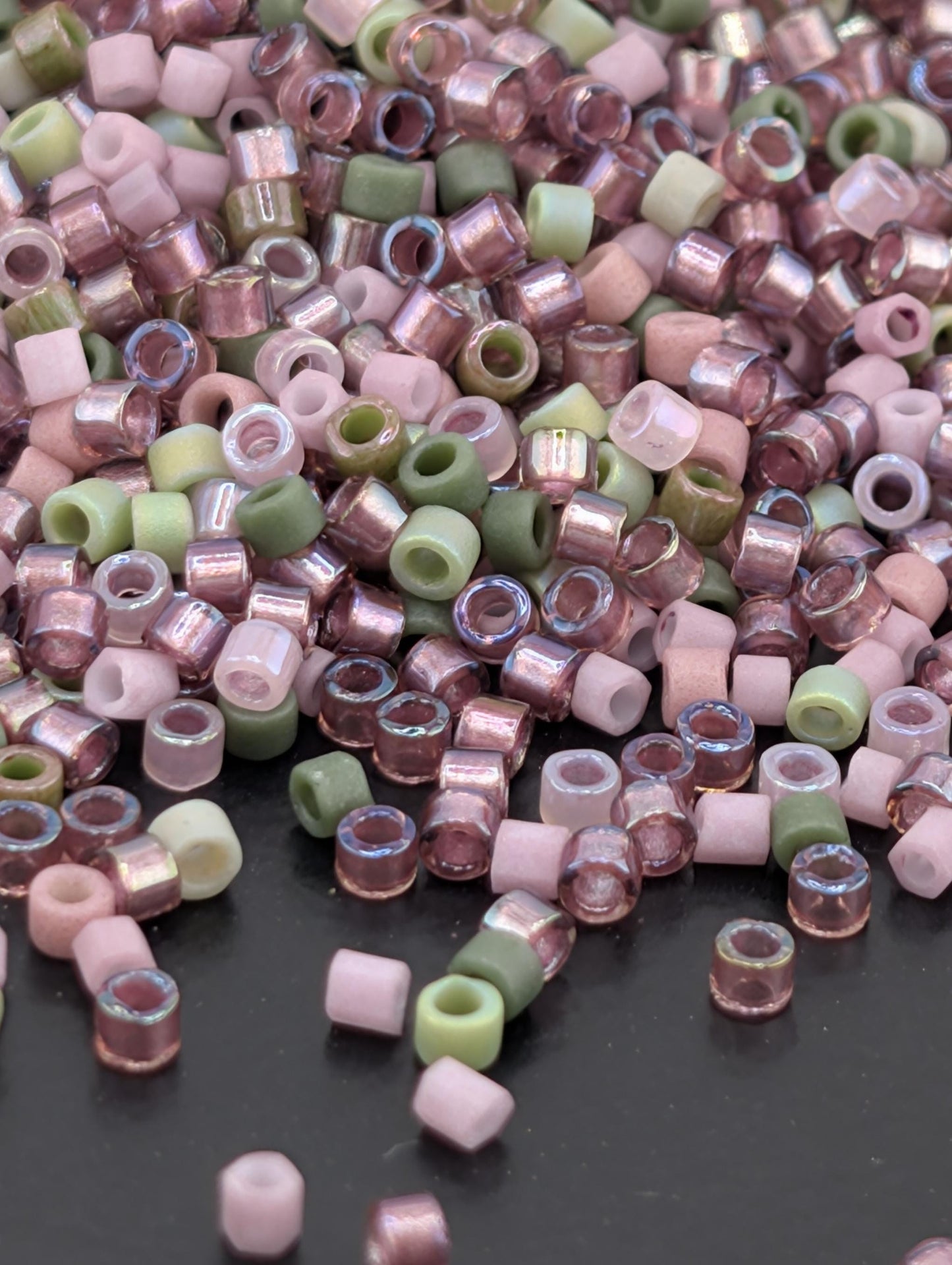 A pile of multicolored glass beads, including pink, green, and white, scattered on a dark surface.