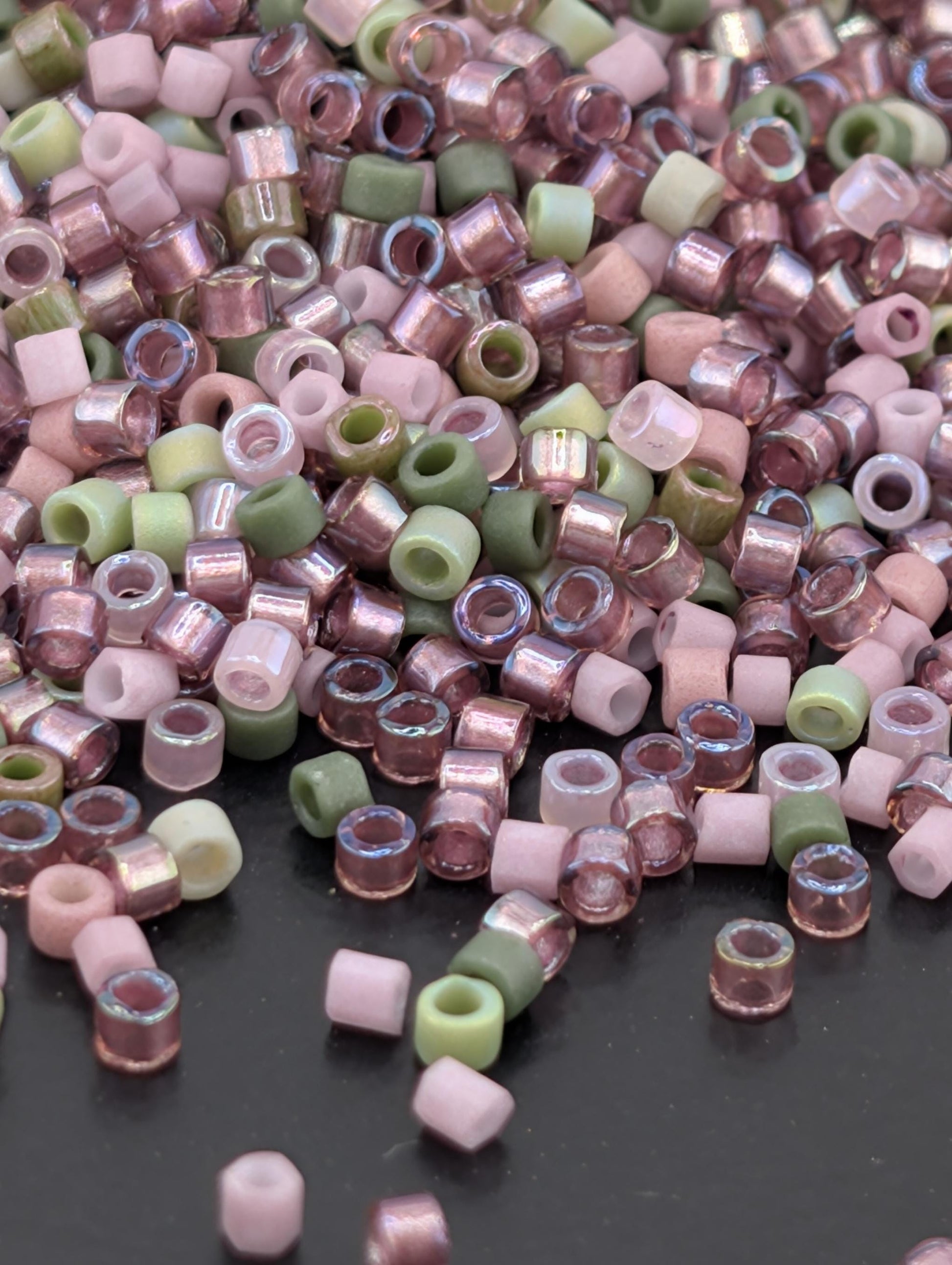 A pile of multicolored glass beads, including pink, green, and white, scattered on a dark surface.