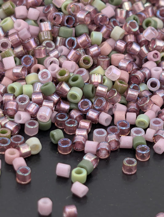 A pile of multicolored glass beads, including pink, green, and white, scattered on a dark surface.
