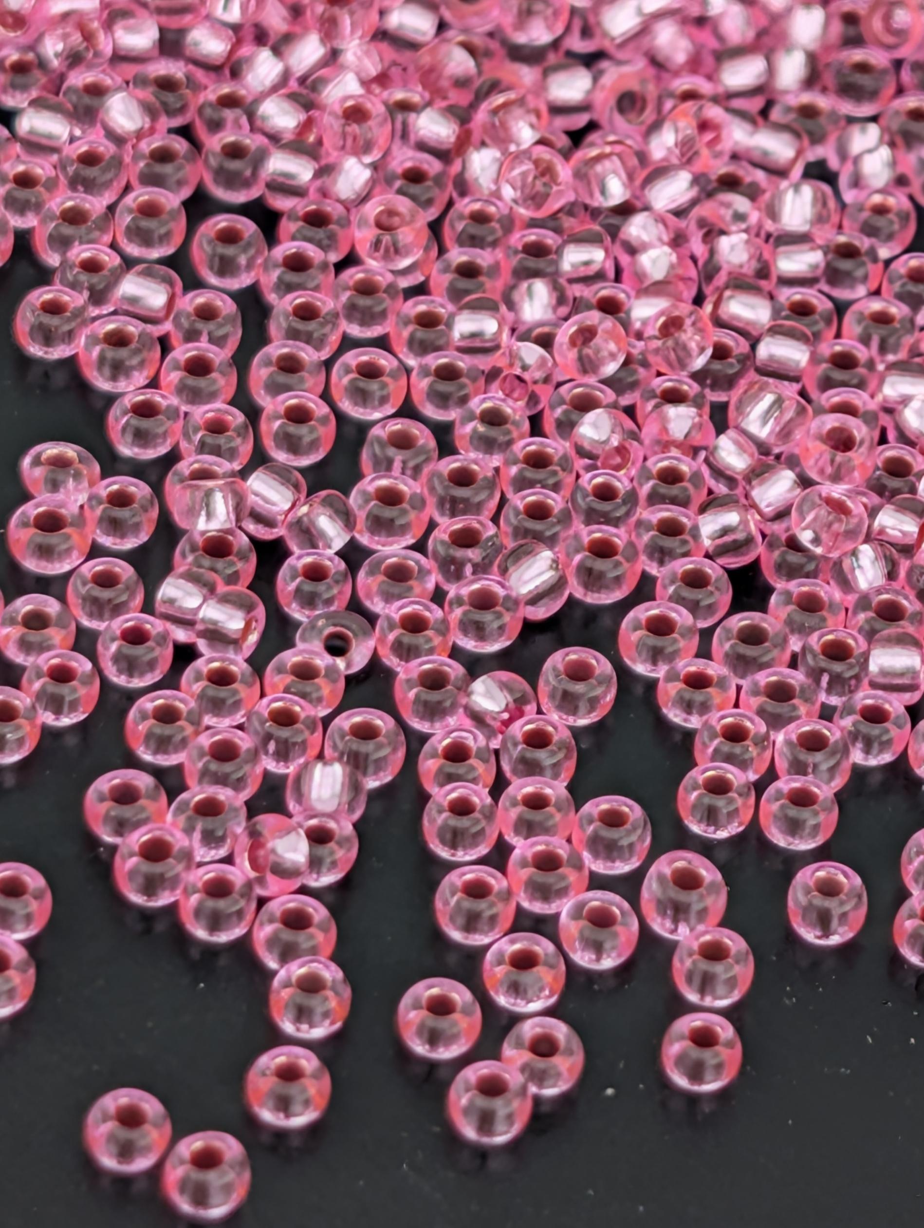a close-up view of numerous small, clear beads in a pink color, scattered across a dark background.