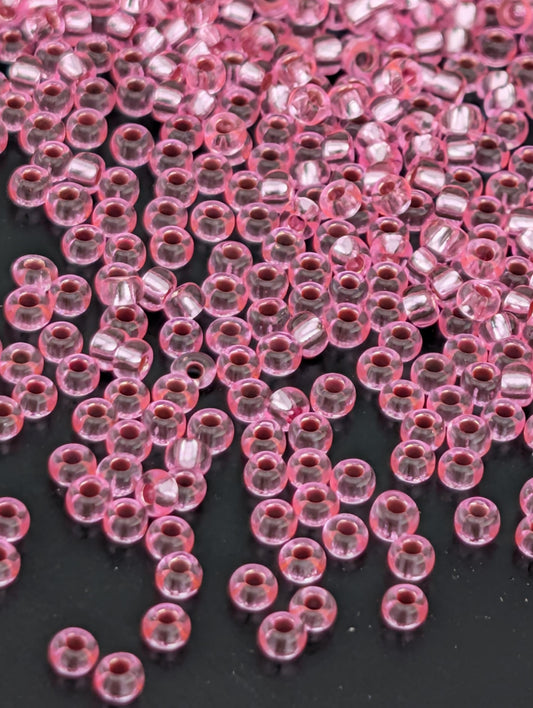 a close-up view of numerous small, clear beads in a pink color, scattered across a dark background.