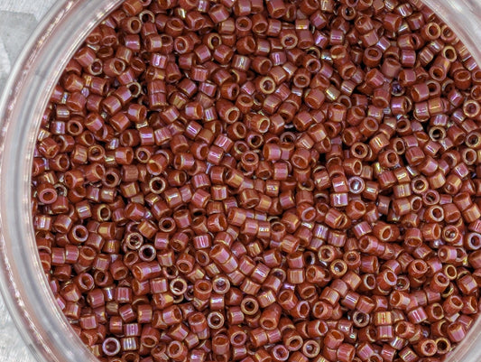 A close-up image of a glass jar filled with numerous small, round beads in a reddish-brown color.