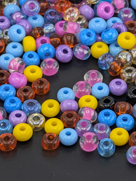 A colorful assortment of multicolored beads, including clear, purple, blue, yellow, and orange, scattered on a dark surface.