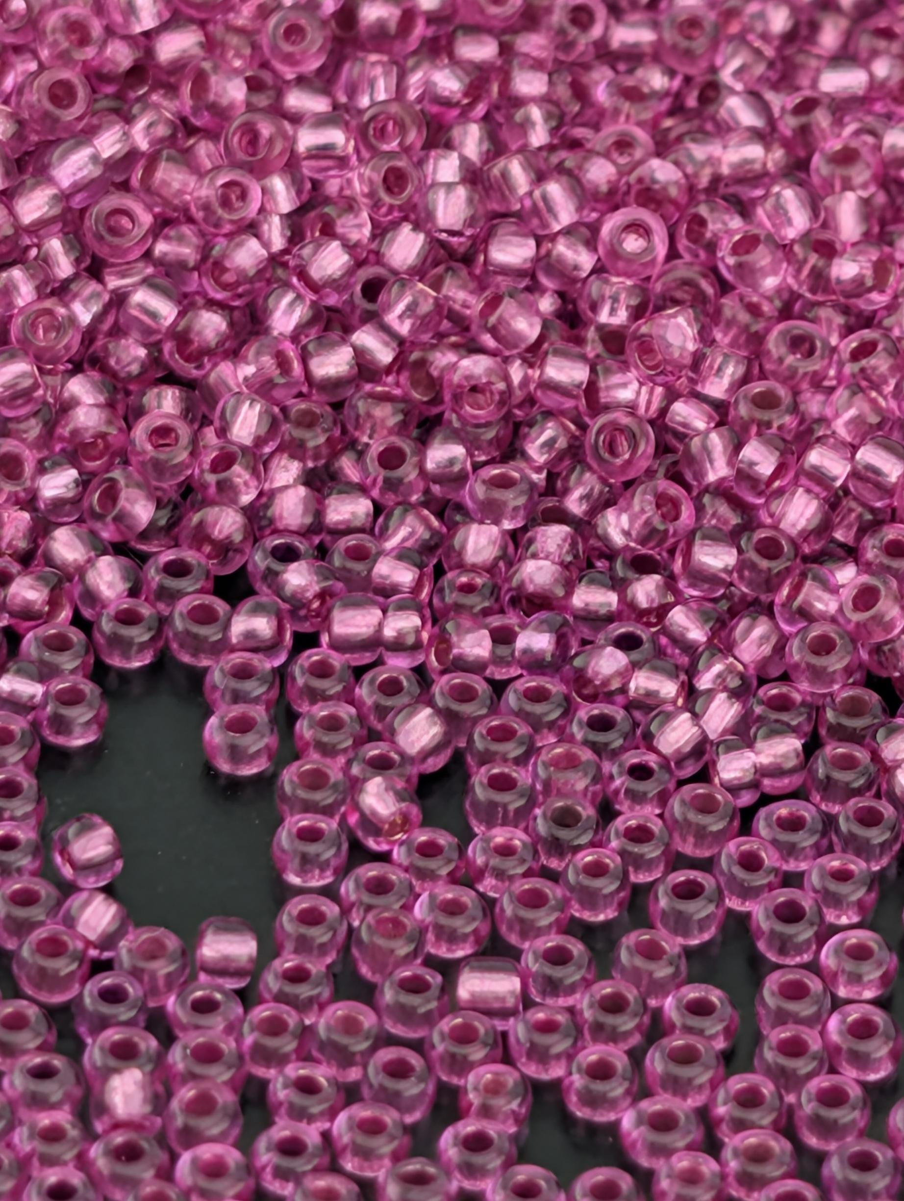 The image is a close-up of numerous small, clear beads in a vibrant shade of pink. The beads are scattered across a dark background, creating a visually striking contrast.