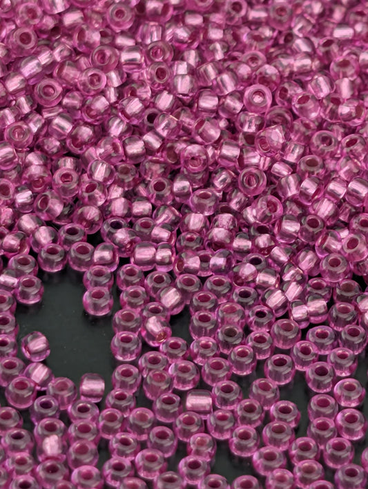 The image is a close-up of numerous small, clear beads in a vibrant shade of pink. The beads are scattered across a dark background, creating a visually striking contrast.