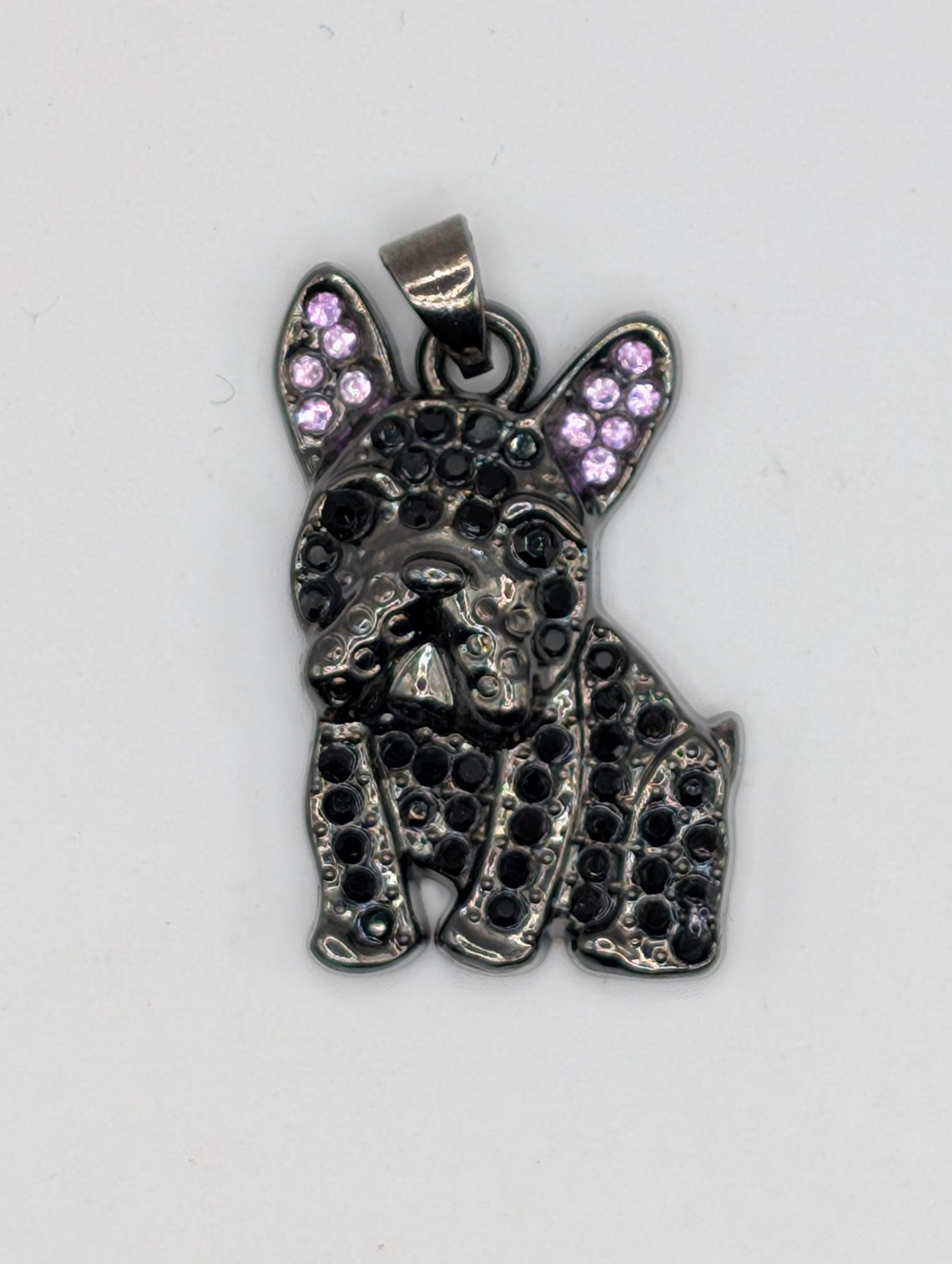 A pendant in the shape of a dog&#39;s head, with a metallic appearance and small purple gemstones or stones embedded in it.