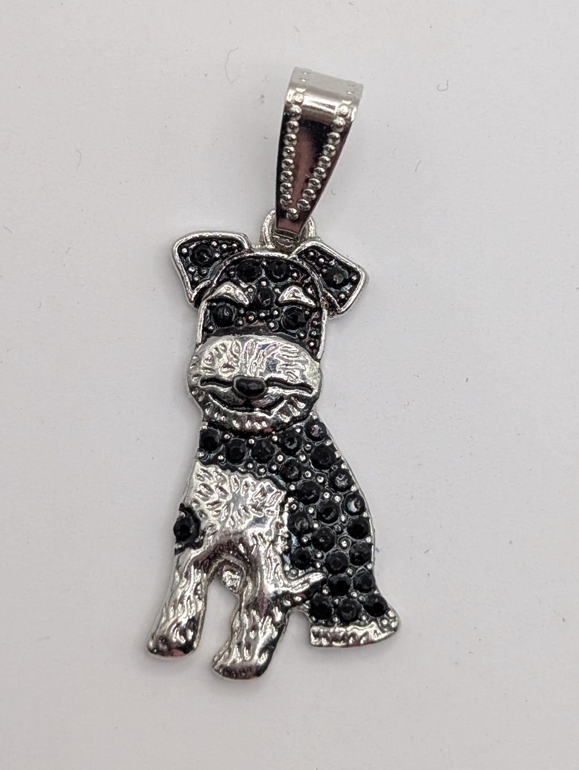 A silver-colored pendant in the shape of a dog, with black rhinestones or crystals adorning it.