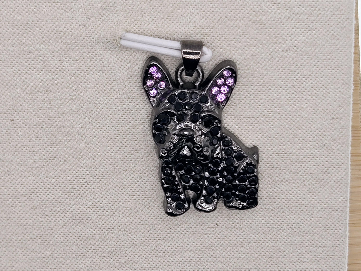 A black pendant in the shape of a dog, adorned with purple gemstones, is displayed on a white fabric surface.