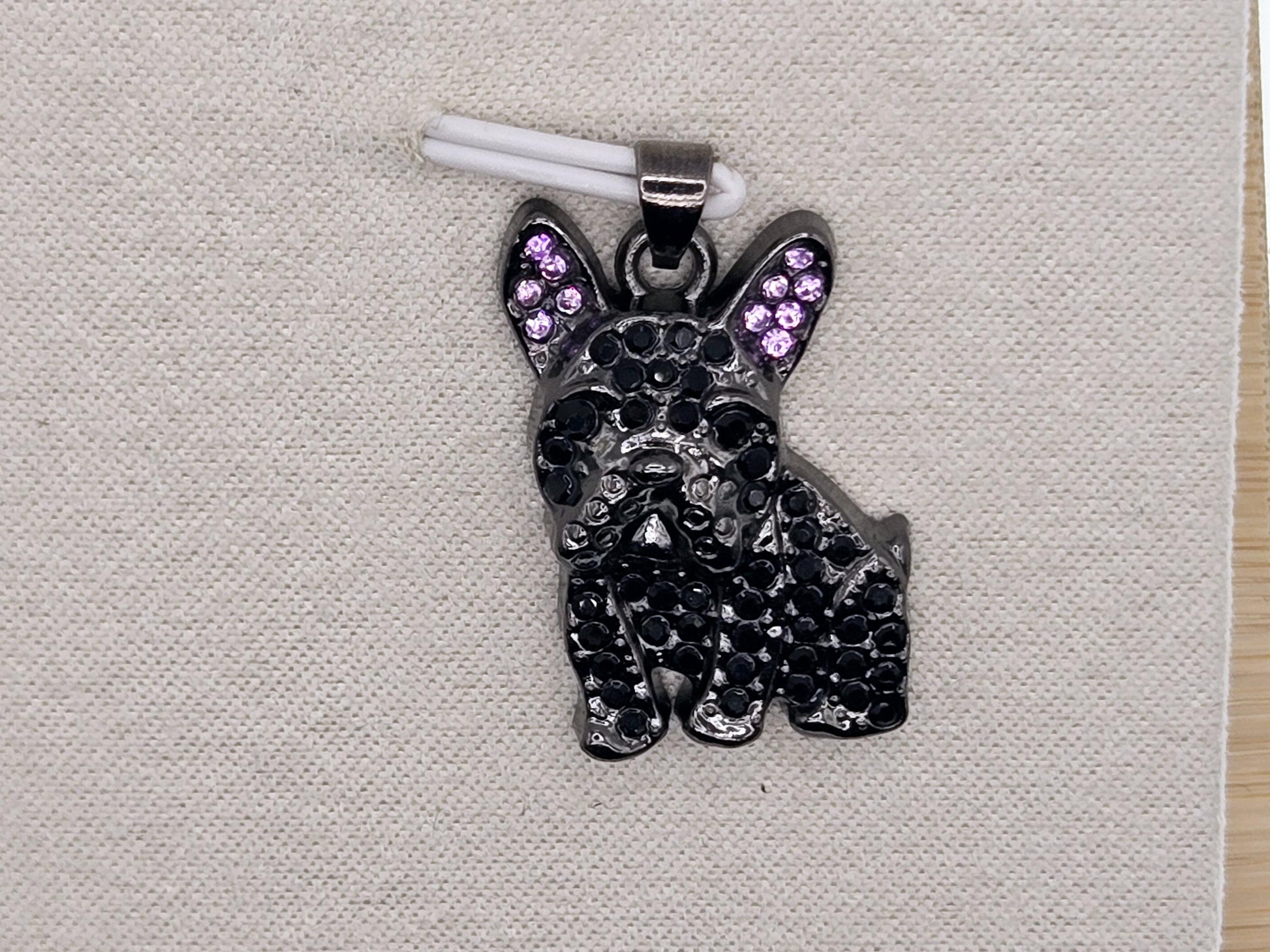 A black pendant in the shape of a dog, adorned with purple gemstones, is displayed on a white fabric surface.