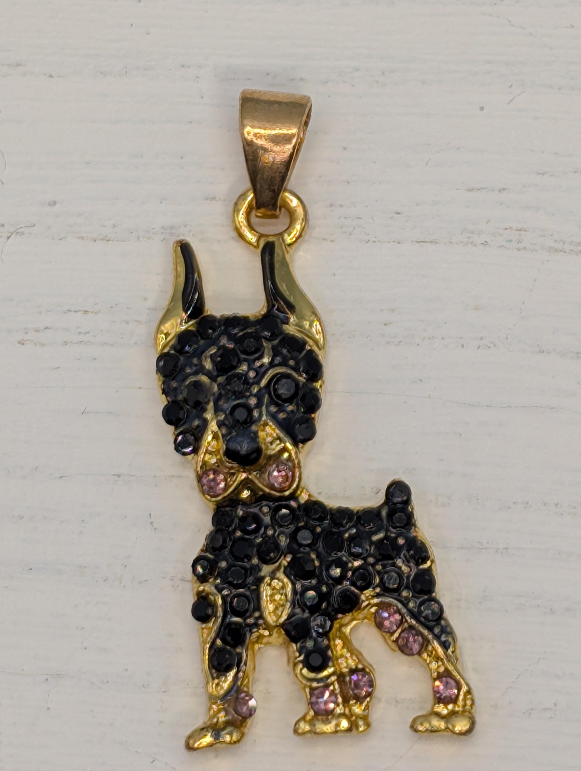 A gold-colored pendant in the shape of a dog, adorned with black rhinestones and purple gemstones.