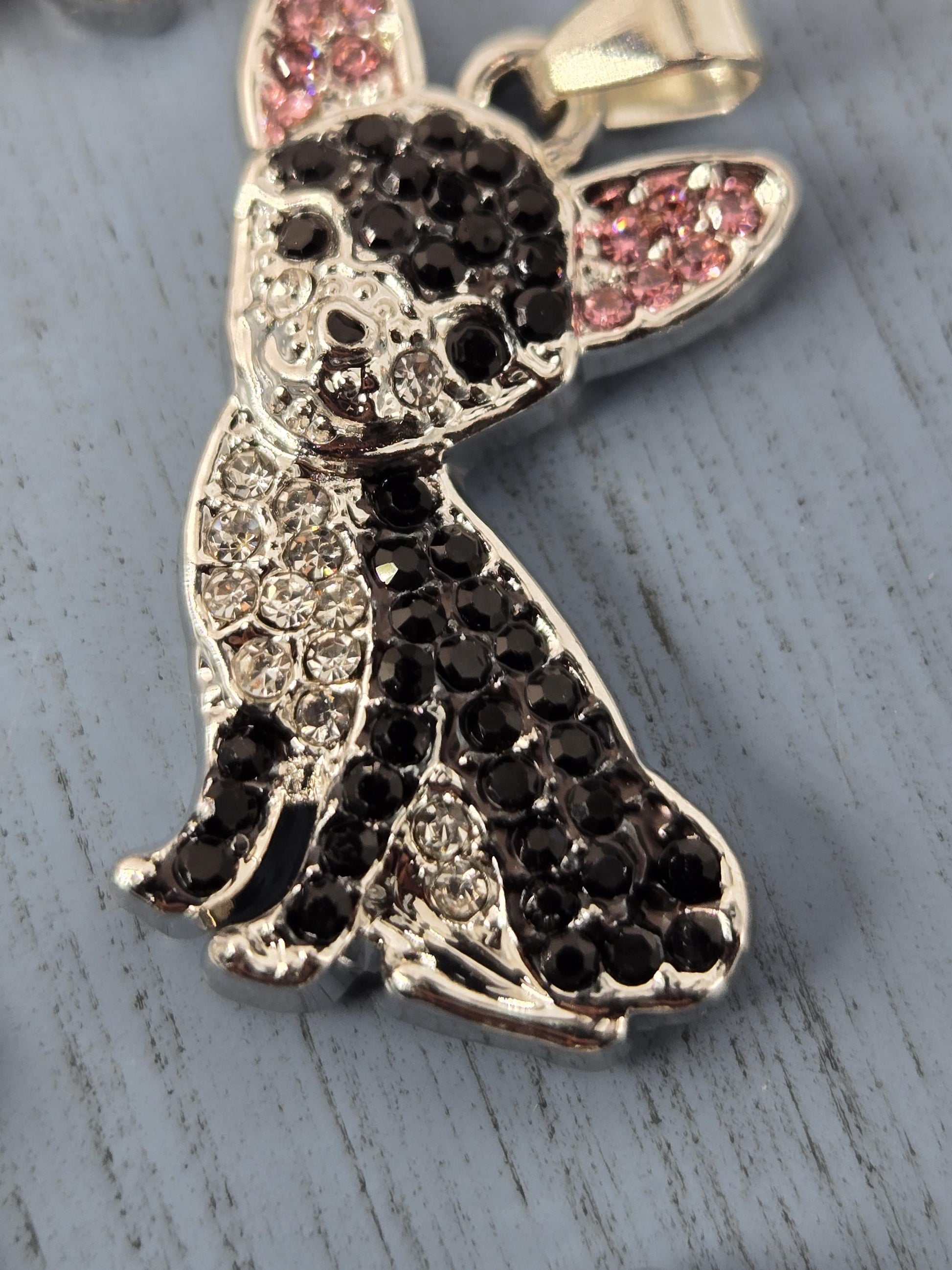 A close-up image of a decorative pendant featuring a stylized design of a bird or bird-like figure, with a combination of black and pink gemstones or crystals adorning the piece.
