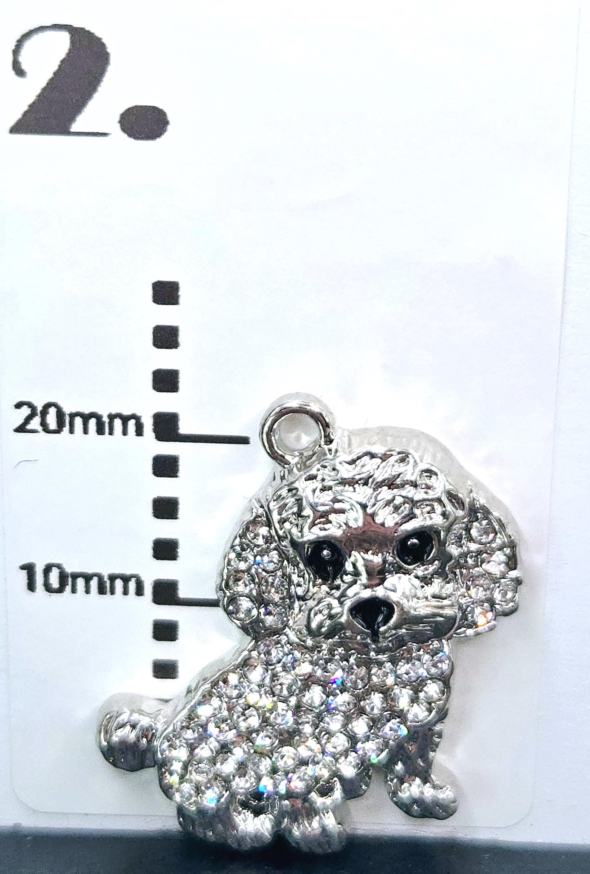 A silver charm in the shape of a poodle, adorned with rhinestones, is displayed against a white background.