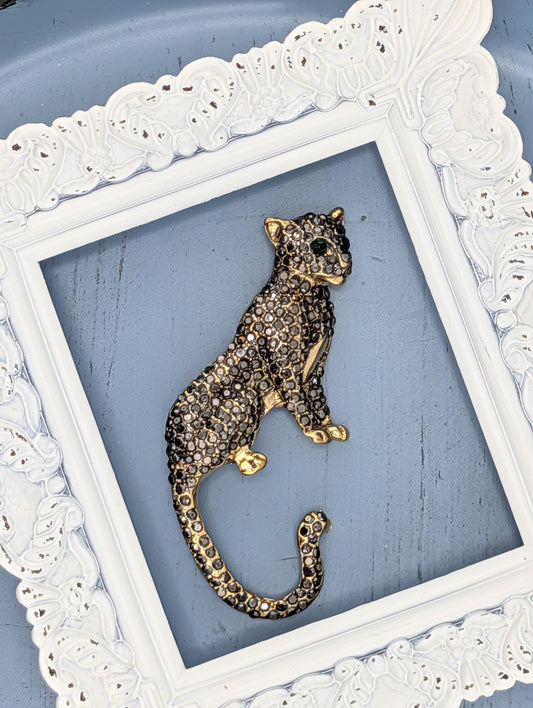 A decorative piece of a leopard-like animal, possibly a cat, is displayed within a white ornate frame against a blue background.