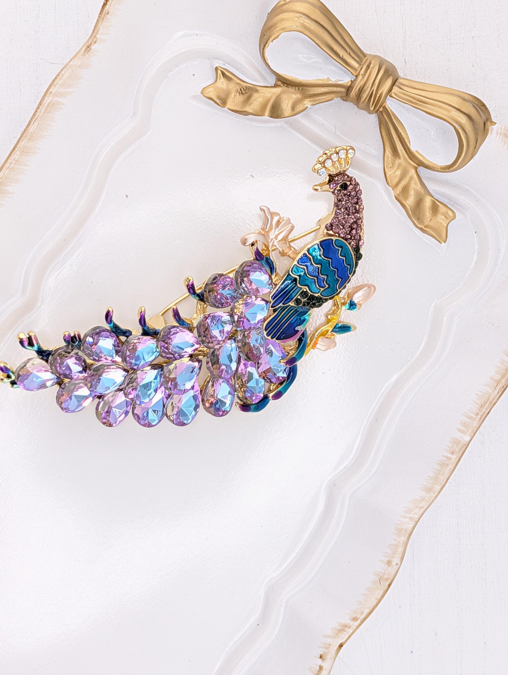 A decorative peacock feather headband with a gold bow and a cluster of colorful gemstones.