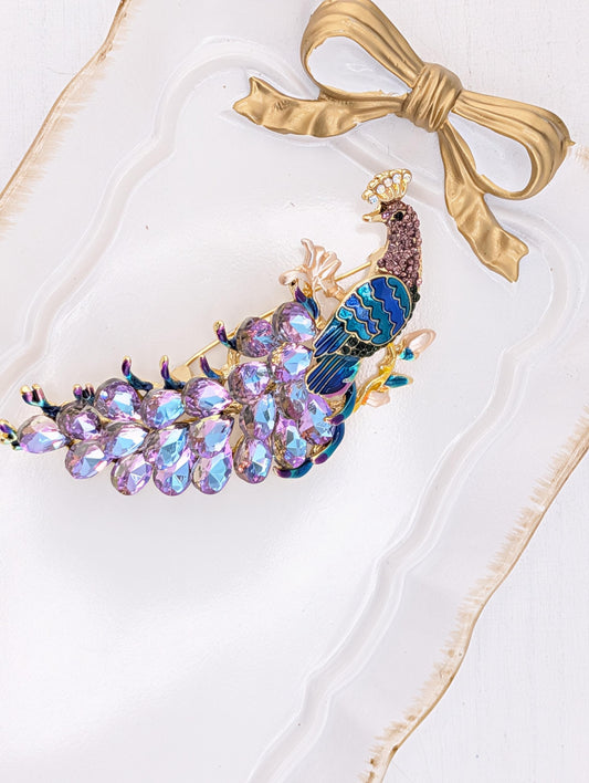 A decorative peacock feather headband with a gold bow and a cluster of colorful gemstones.