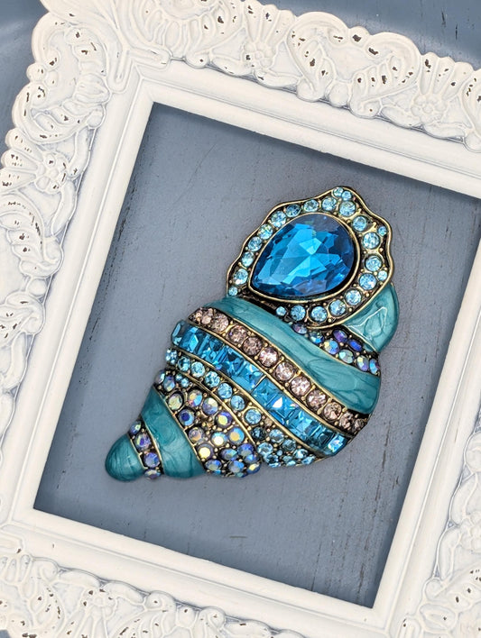 A decorative blue and gold brooch with a large blue gemstone is displayed in a white ornate frame.