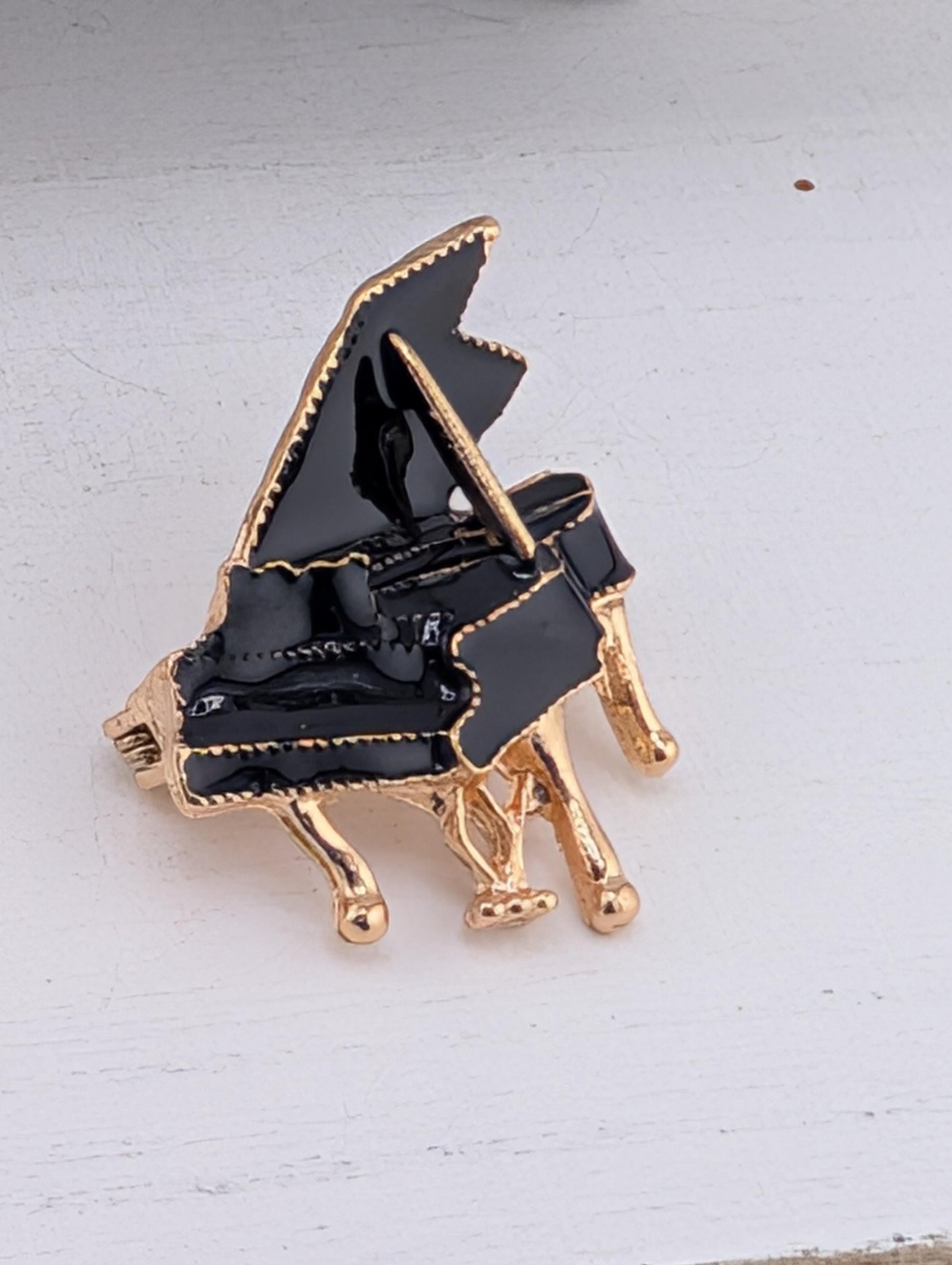 A black and gold piano brooch is displayed on a white surface.