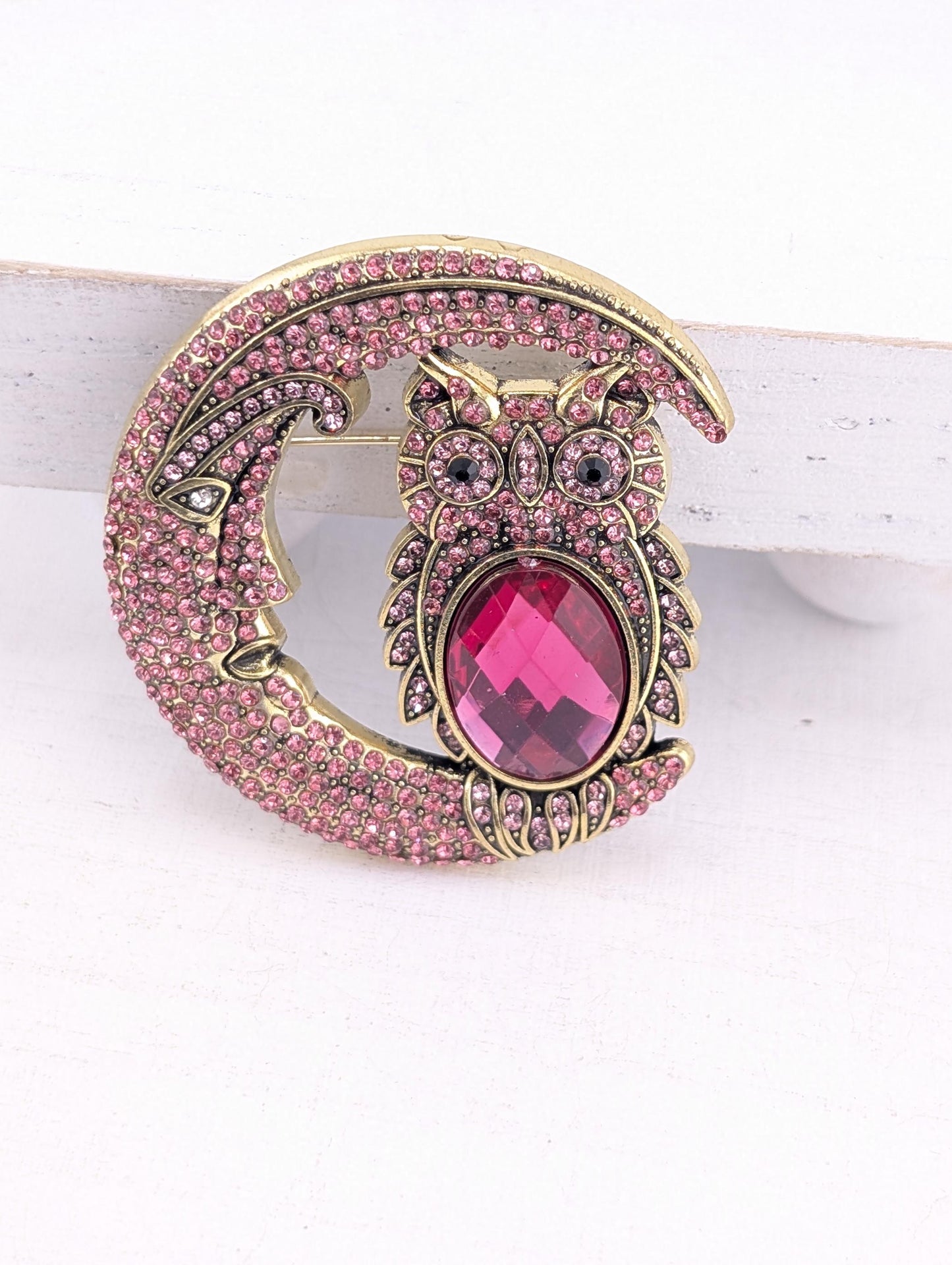 A decorative brooch in the shape of a crescent moon, with a large pink gemstone in the center.