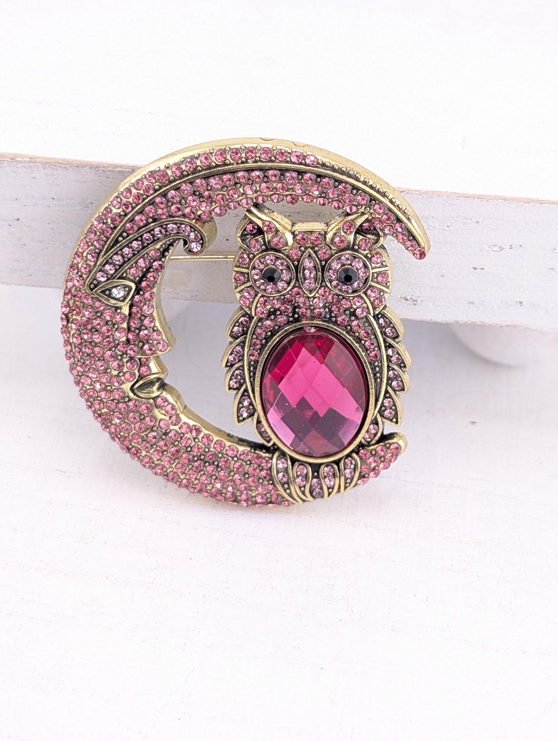 A decorative brooch in the shape of a crescent moon, with a large pink gemstone in the center.