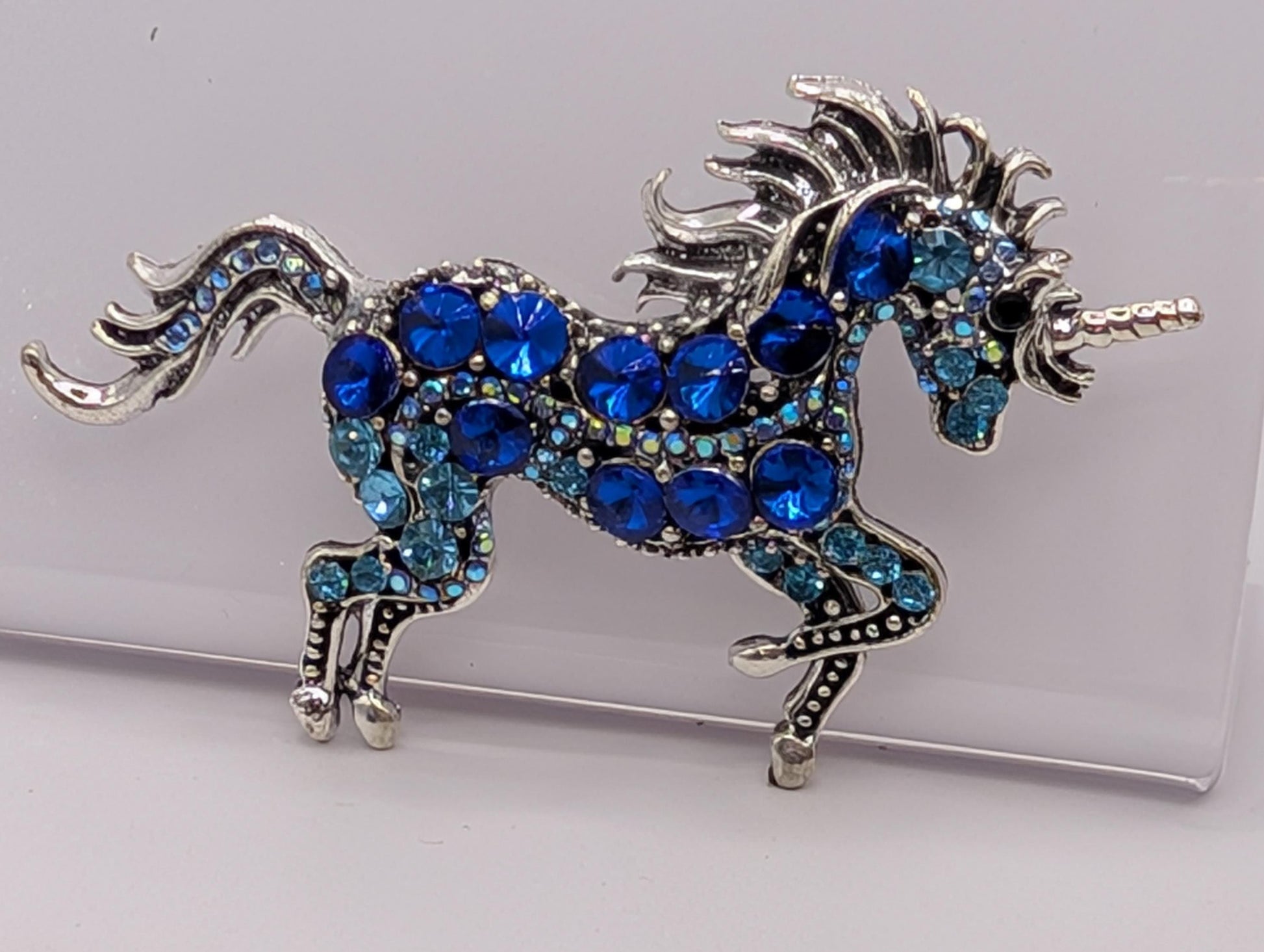 A decorative brooch in the shape of a unicorn, adorned with blue gemstones and silver details.